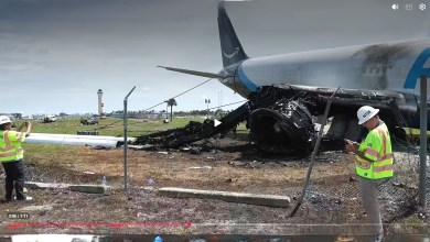 NTSB investigators wearing yellow hard hats and vests walk around the damaged Amazon Prime Air jet that overran the runway in Miami.