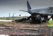 NTSB investigators wearing yellow hard hats and vests walk around the damaged Amazon Prime Air jet that overran the runway in Miami.