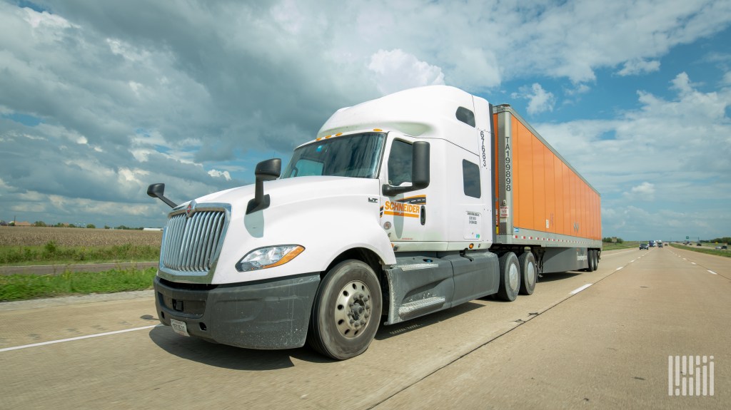 a white Schneider sleeper cab pulling an orange Schneider trailer on a highway
