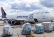 A blue-tailed Kuehne+Nagel 747 jumbo jet freighter at an airport with cargo pallets on the ground ready to be loaded.