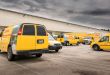 Yellow DHL Express vans are spread out in a company parking lot.