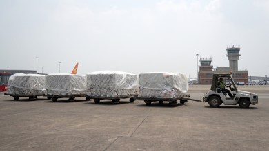A tug pulls carts with cargo pallets across the tarmac at an airport on a gray day.