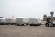 A tug pulls carts with cargo pallets across the tarmac at an airport on a gray day.