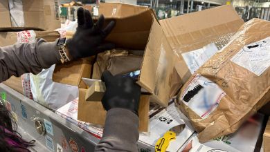 An inspector rips open a package on a U.S. Postal Service conveyor belt full of packages.