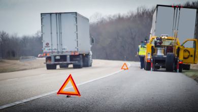 A truck out of service along the side of a highway with a service technician truck and warning beacons placed along the roadside edge