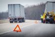 A truck out of service along the side of a highway with a service technician truck and warning beacons placed along the roadside edge