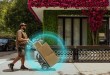 A UPS driver in a brown uniform pushes a handtruck with a large box on a sidewalk.
