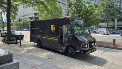 A brown UPS truck parked on a shaded city street, as seen from the side.