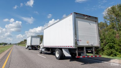 Two white box trucks on a highway, illustrating box truck carrier TLA Group’s move to over-the-road freight