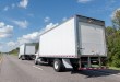 Two white box trucks on a highway, illustrating box truck carrier TLA Group’s move to over-the-road freight