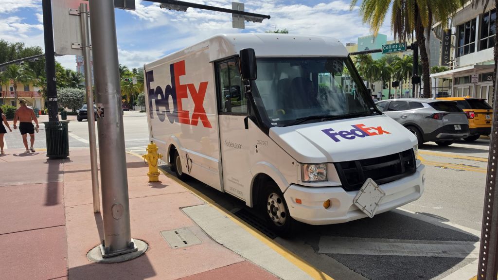 A FedEx van parked at a street corner in Miami Beach on a sunny day, with palm tree in the background.