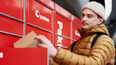 A man with a wool hat removes a package from a red parcel locker unit.